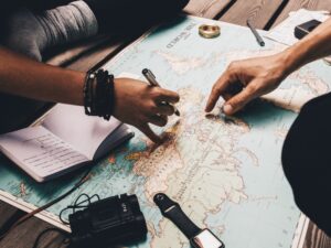 Close up view of man and woman pointing at places on world map. Woman noting vacation plan in a diary.