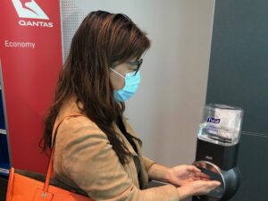 Passenger wearing face mask uses hand sanitiser at Qantas boarding gate
