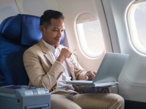 Elegant businessman using laptop while sitting in airplane cabin with sun shining trough airplane window.