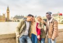 Happy multiracial friends group using smartphone in London. Mixed race millennials people lifestyle concept. Friends sharing trip on social network. Big ben and Westminster parliament on background.