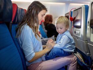 Mother, entertaining little toddler boy on board of aircraft on a long distance international flight, while traveling to a holiday