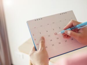 Hand with pen mark at 12th on calendar date with red circle