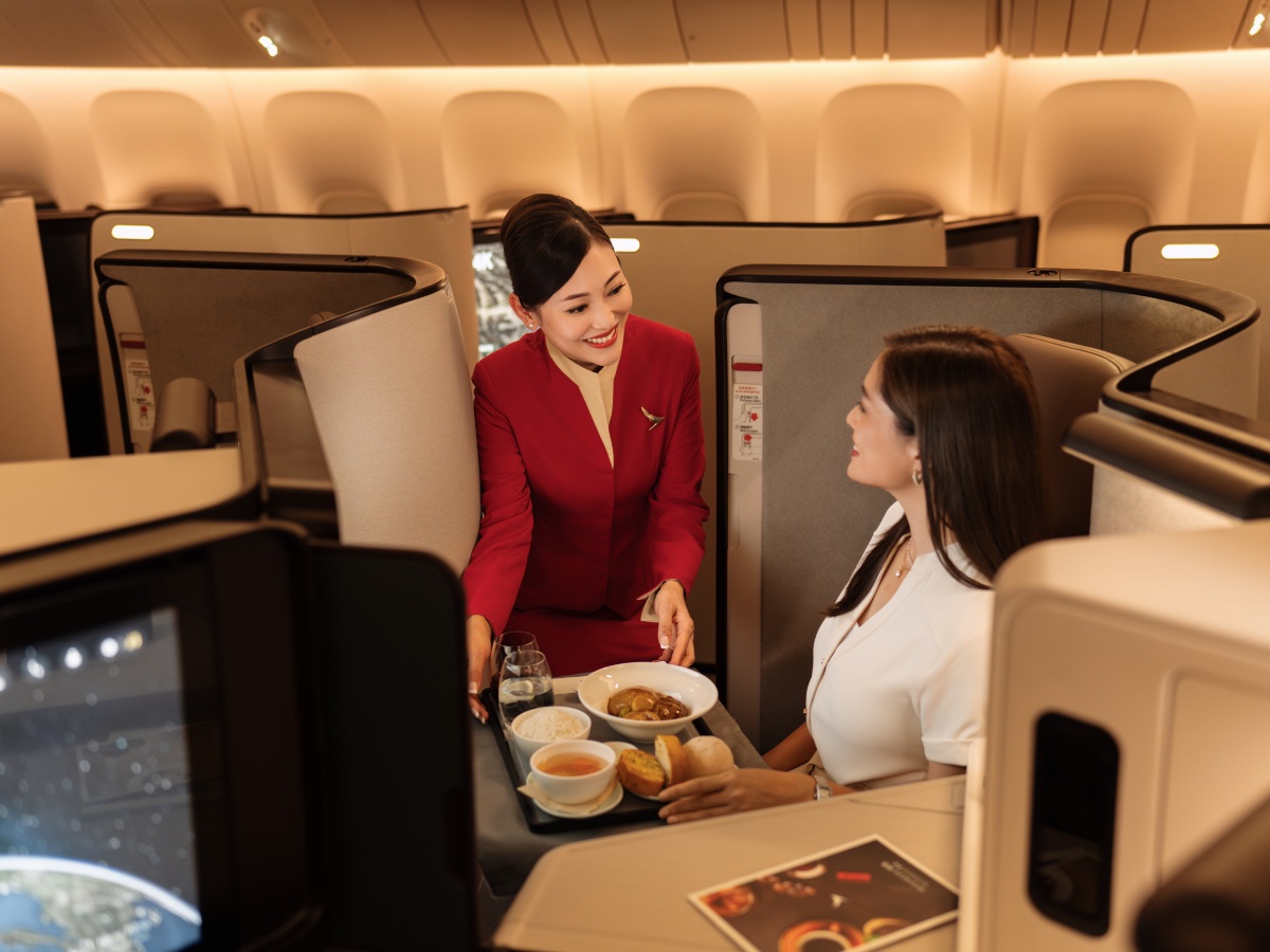 Cathay Pacific Aria Suite business class flight attendant serving a meal