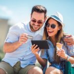 Happy couple paying on line with credit card and digital tablet on the street