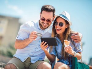 Happy couple paying on line with credit card and digital tablet on the street