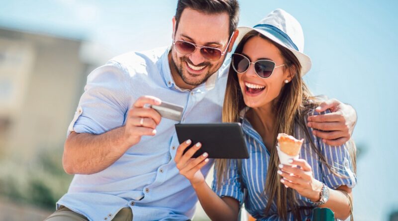 Happy couple paying on line with credit card and digital tablet on the street