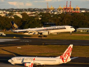 A Singapore Airlines A350 lands at Sydney Airport on runway 25 with a Virgin Australia 737 in foreground