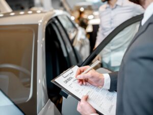 Manager filling car rental documents standing in the showroom with car on the background