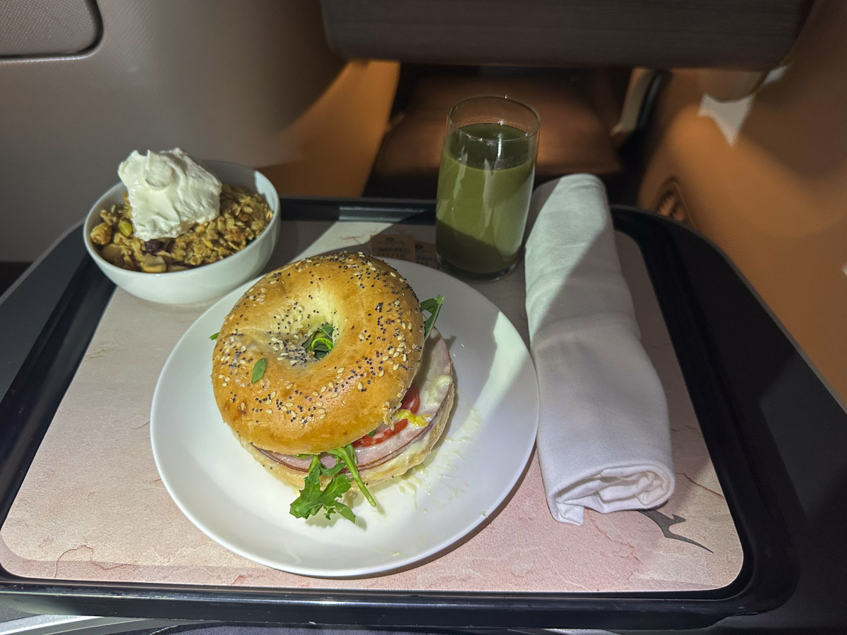 An everything bagel with melted Gruyere cheese, ham, tomato, rocket and fried egg, with Brookfarm macadamia toasted muesli for breakfast in Qantas business class