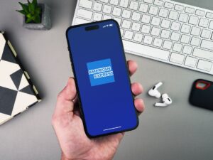 Man holding a smartphone with American Express Amex app on the screen on grey background table. Office environment