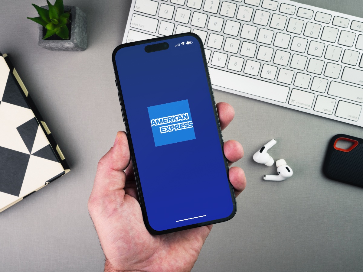 Man holding a smartphone with American Express Amex app on the screen on grey background table. Office environment
