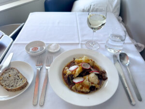 Spanner crab tortellini with oxtail, rosemary jus and skordalia in Qantas first class, with bread and a glass of white wine