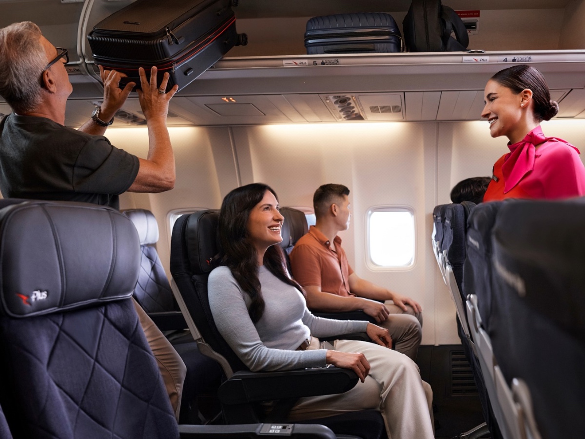 Qantas Economy Plus seats on a Boeing 737 with flight attendant and passenger stowing carry-on bag