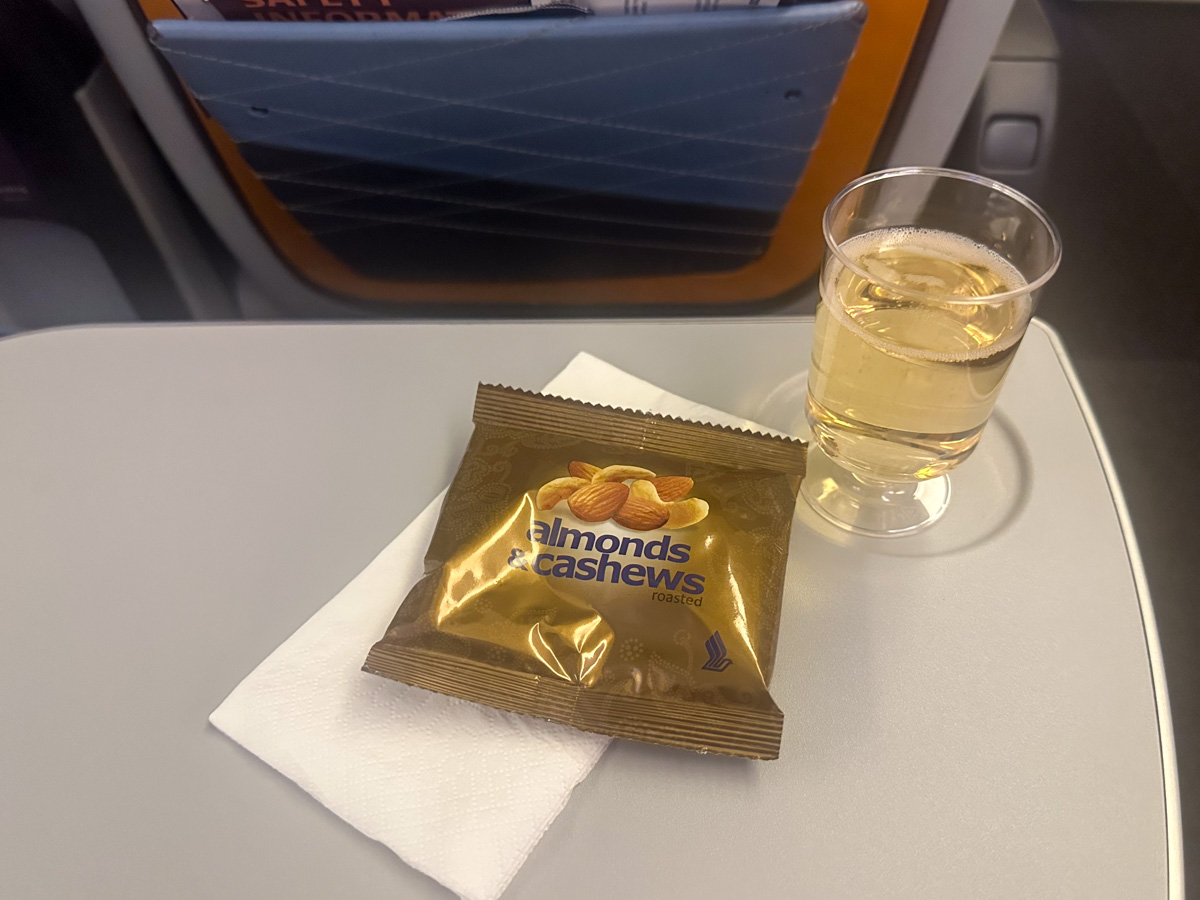 Singapore Airlines premium economy champagne, served in a plastic cup with nuts