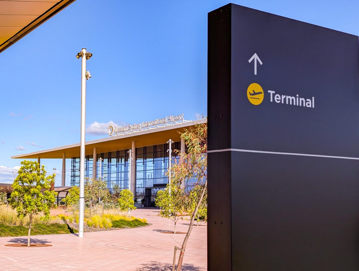 Glass entrance of the Western Sydney International Airport terminal with concrete columns, native gardens and a Terminal sign