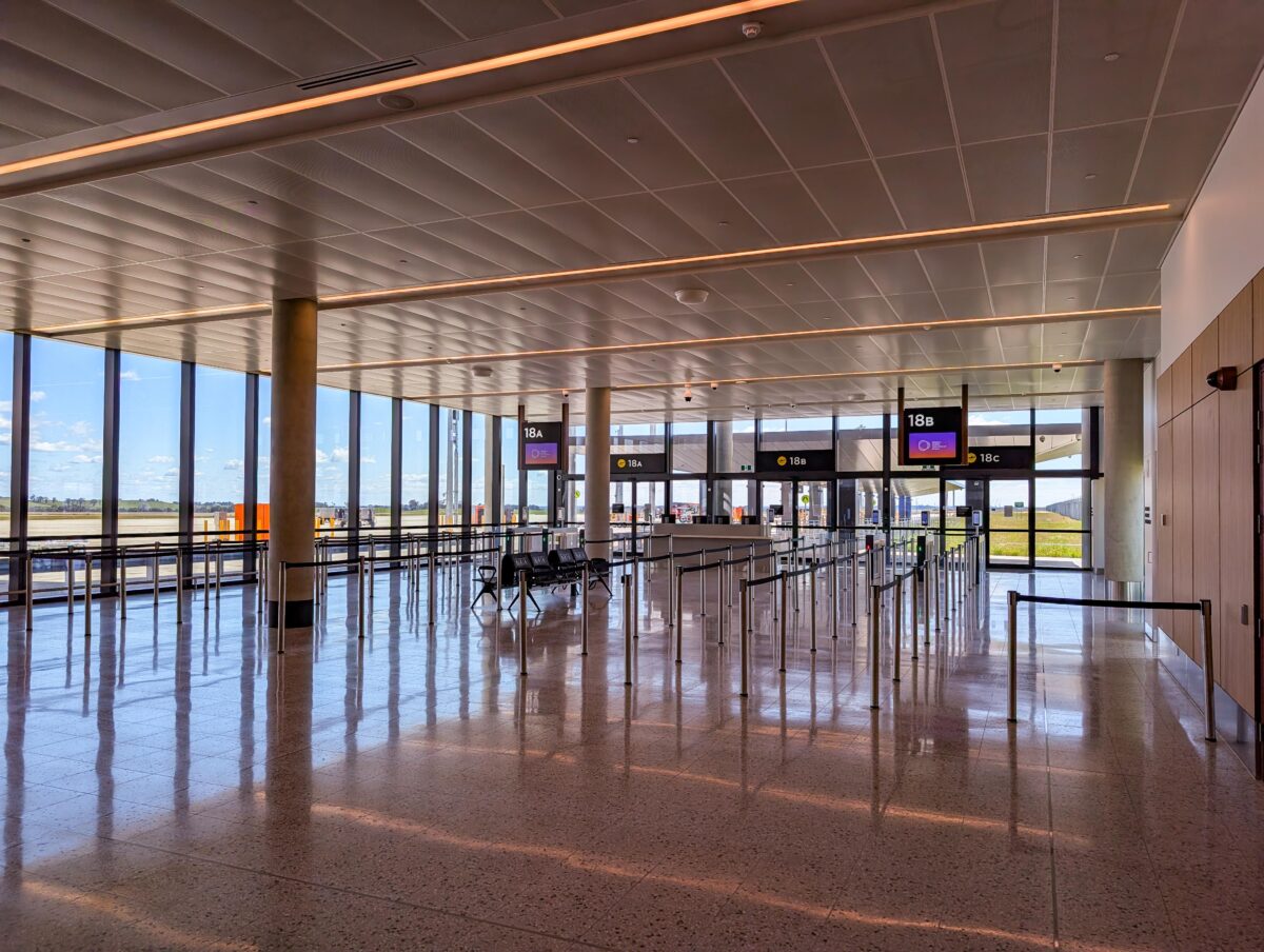 Empty boarding area for gates 18A, 18B and 18C with queue barriers and glass doors to the apron