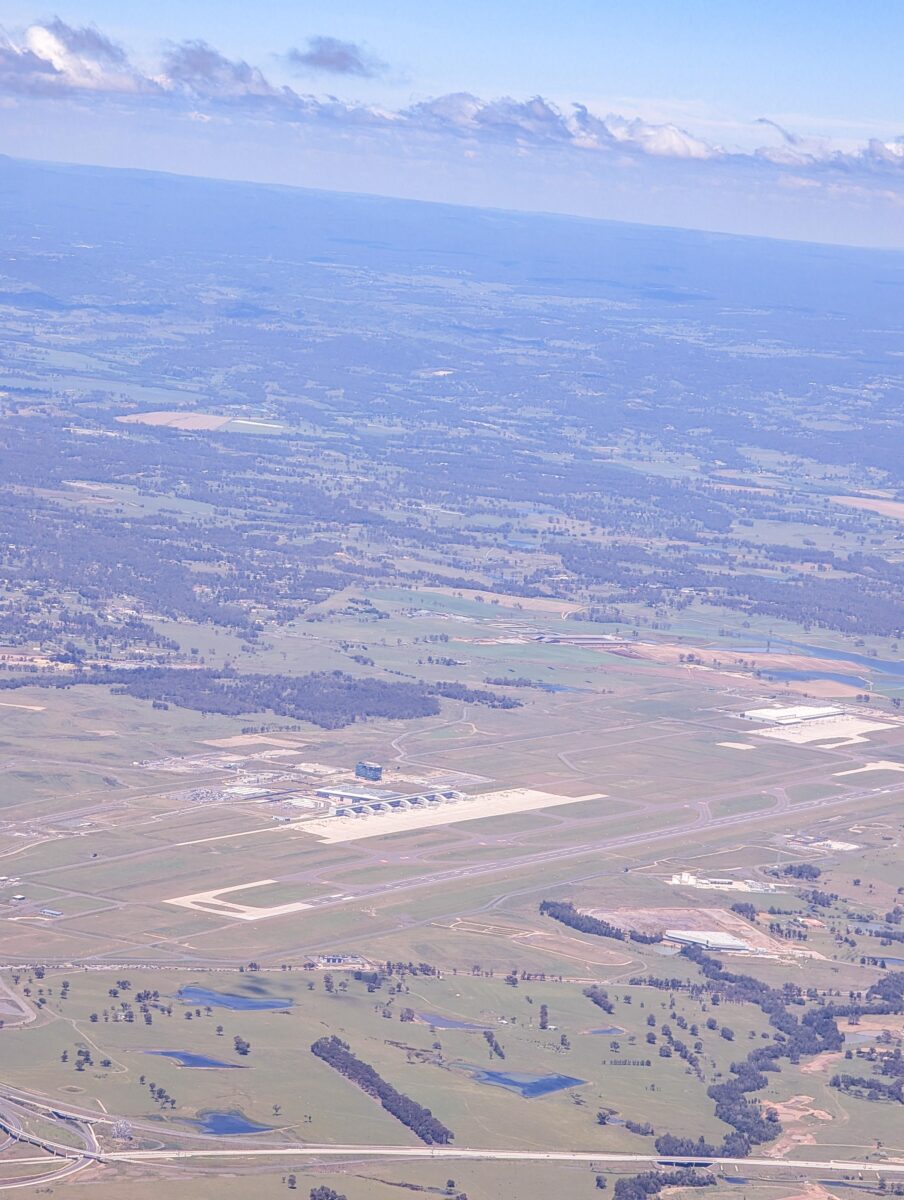 Aerial view of Western Sydney International Airport showing the terminal, apron and runway surrounded by farmland